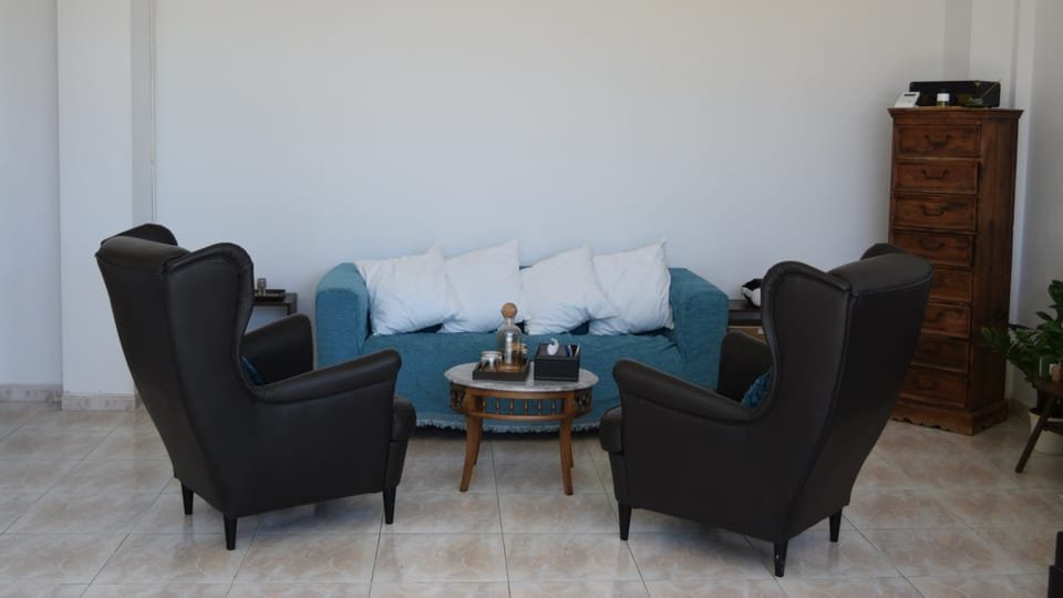Sala de consulta con dos sillones enfrentados, sofá azul y mesita de mármol